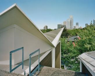 A photograph of a view from the roof of a school, with trees and apartment buildings in the bac…