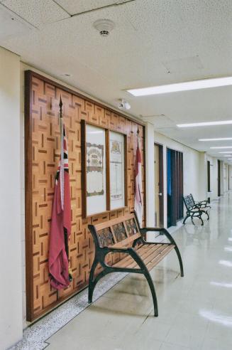 A photograph of a hallway inside a public school, with benches and a display panel.