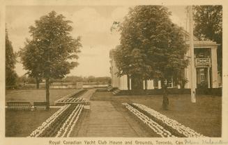 Sepia toned photograph of a large building in manicured grounds with a lagoon in the background…