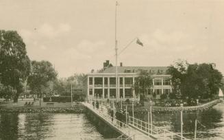 Black and white photograph of a people walking across a bridge towards a large building.