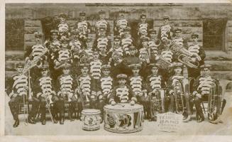 Black and white photograph of four rows of men in marching band uniforms posing with their inst…