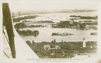 Black and white photograph shot from a plane of lagoons and land with a few buildings. Lighthou…