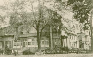 Black and white photograph of a three story Victorian home with a long verandah.