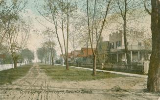 Colorized photograph of a row of cottages along a sandy tree lined street.