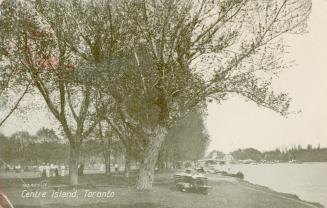 Black and white photograph of people enjoying a summer day on an island; water to the right.