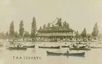 Black and white photographs of many canoes in the water in front of a three story Victorian bui…