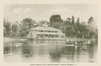 Black and white picture of people in a row boat in the water in front of a two story club house…