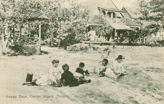 Black and white photograph of five children playing in the sand in front of two Victorian cotta…