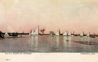 Many sailboats stand at anchor in the water of a large lake.