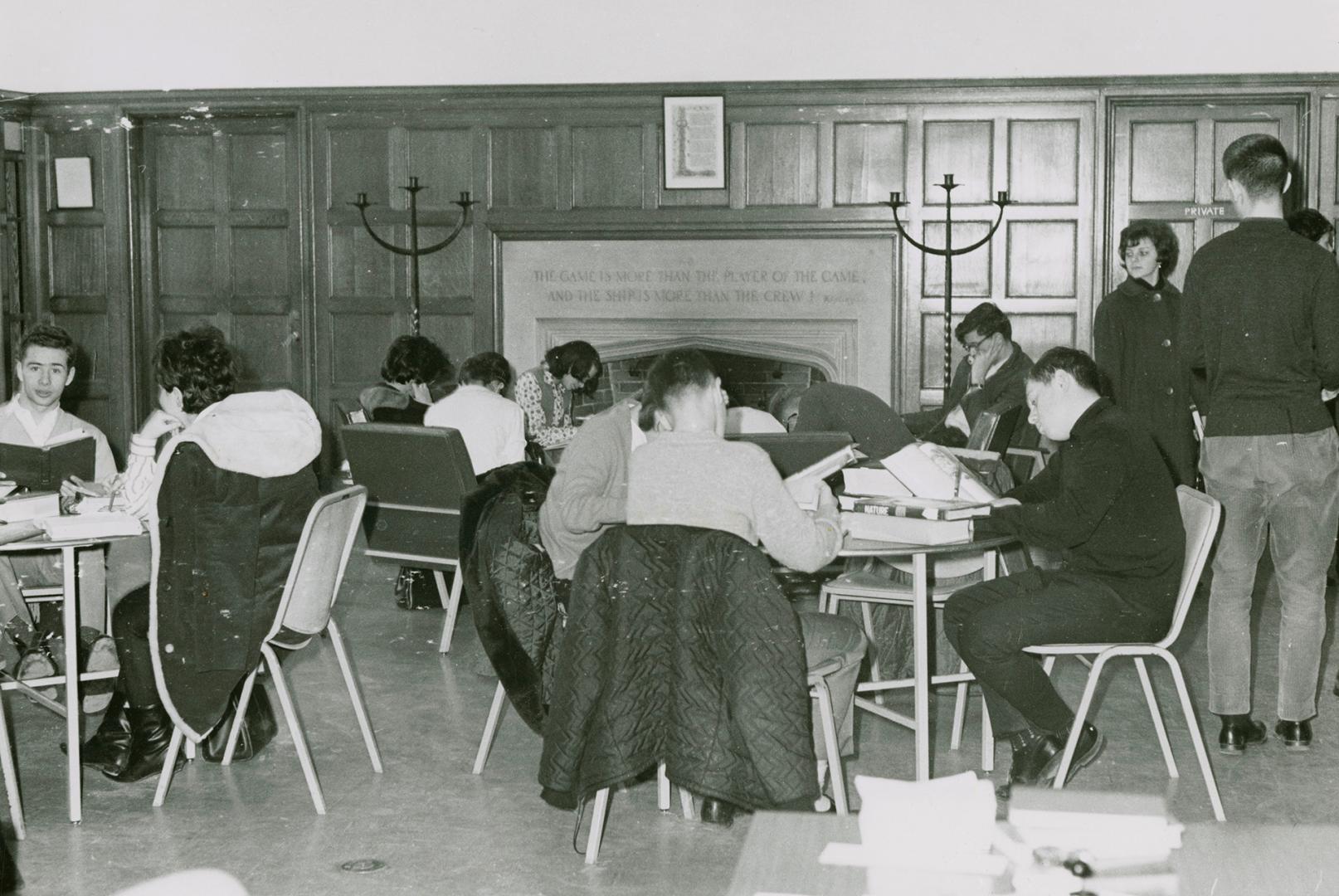 Black and white picture of tables with students sitting and studying in a library room with woo…