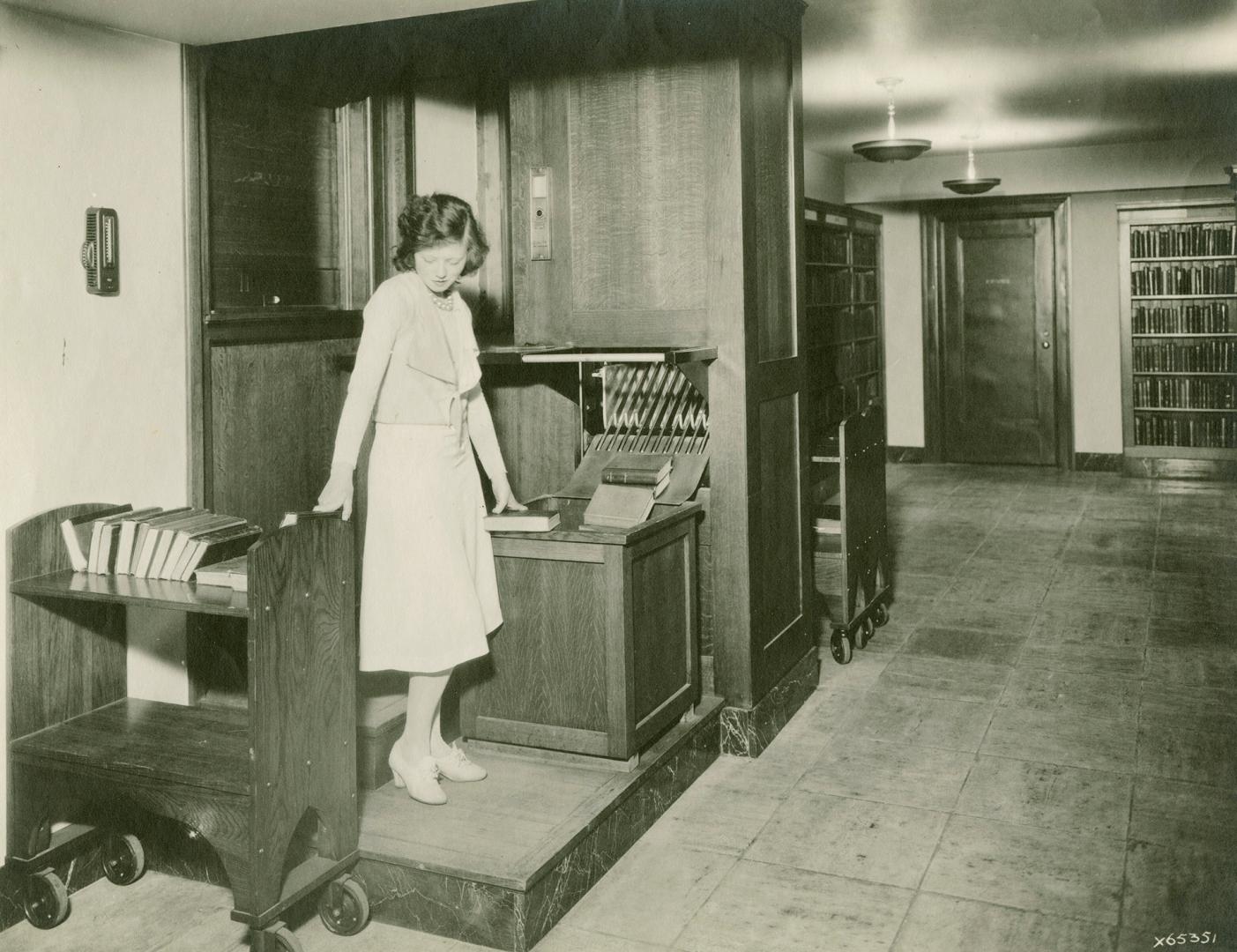 Woman operating library book conveyor moving a book from conveyor to book truck. 