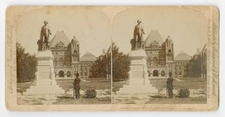 Pictures show a man looking at a bronze stature of a man on a pedestal in front of a very large…