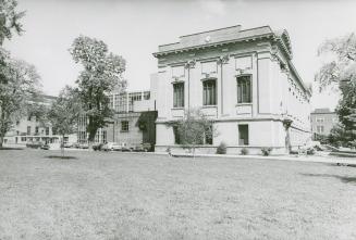 Library building with three large windows and parking lot and large lawn in foreground.