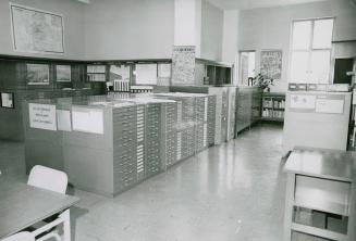 Library room filled with map cabinets and some shelves along the walls and maps displayed on wa…