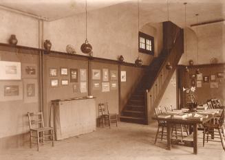 A photograph of a room with a table and chairs in the middle of it. There are books and magazin…