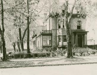 Photo of two story Victorian house surrounded by leafy trees.