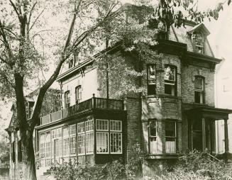 Photo of two story brick Victorian House surrounded by leafy trees.