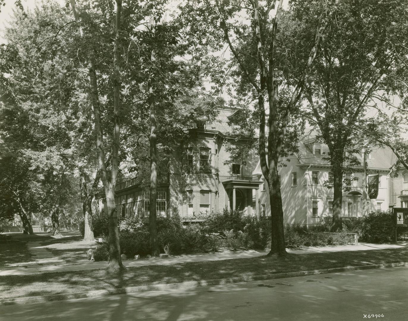 Photo of street with two houses surrounded by leafy trees.