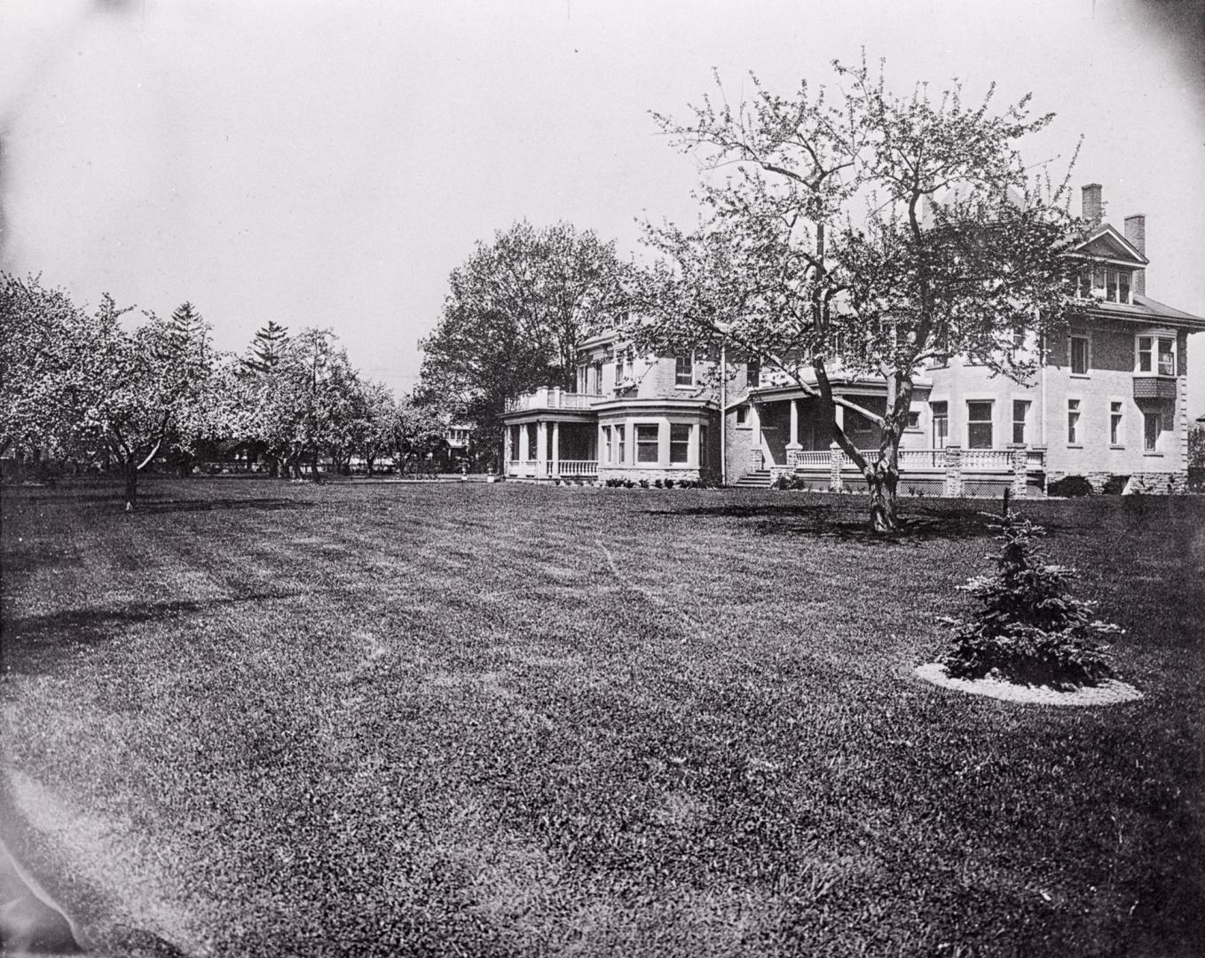 Shows a large three storey house with multiple chimneys and verandahs, surrounded by deciduous …