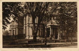 Sepia toned picture of a large house with bay windows and a balcony covering the front door.
