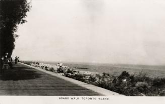 Black and white photograph of a wooden sidewalk beside a body of water.
