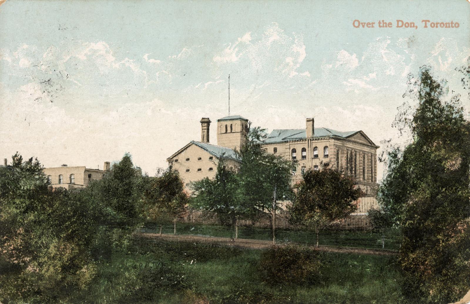 Colorized photograph of a large Victorian jail building as seen in the distance across a river.…