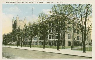 Colorized picture of a four story Collegiate Gothic building with a fence and a row of trees in…