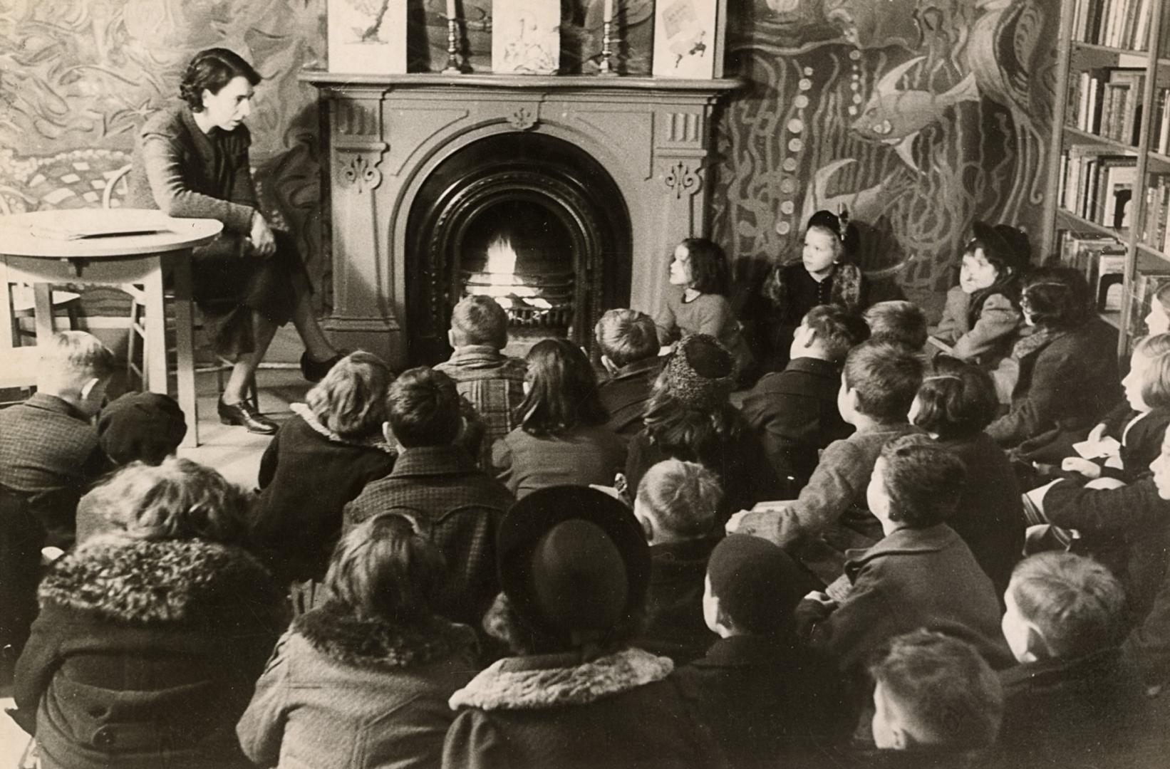 Picture of a librarian telling a story to a group of children seated on the floor gathered arou…