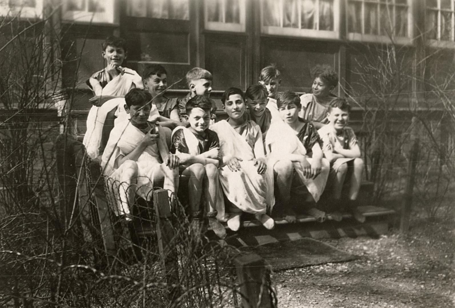 Picture of a group of boys and an adult dressed up for a play and sitting on the steps of the l…