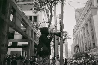 A photograph of a person speaking through a megaphone to a large group of people sitting and st…