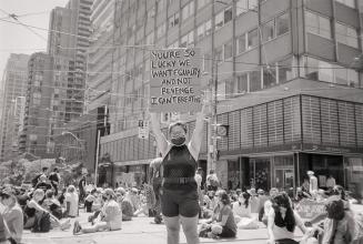 A photograph of a young adult standing on a street and holding up a sign reading &quot;YOU'RE S…