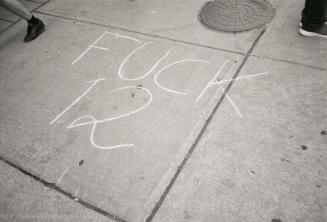 A photograph of a message reading &quot;FUCK 12&quot; written in chalk on a road. A maintenance…