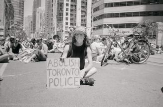 A photograph of a young adult sitting in the middle of a road which is surrounded by tall build ...