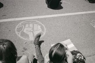 A photograph of a chalk illustration of a clenched first within a circle, drawn on a paved road…