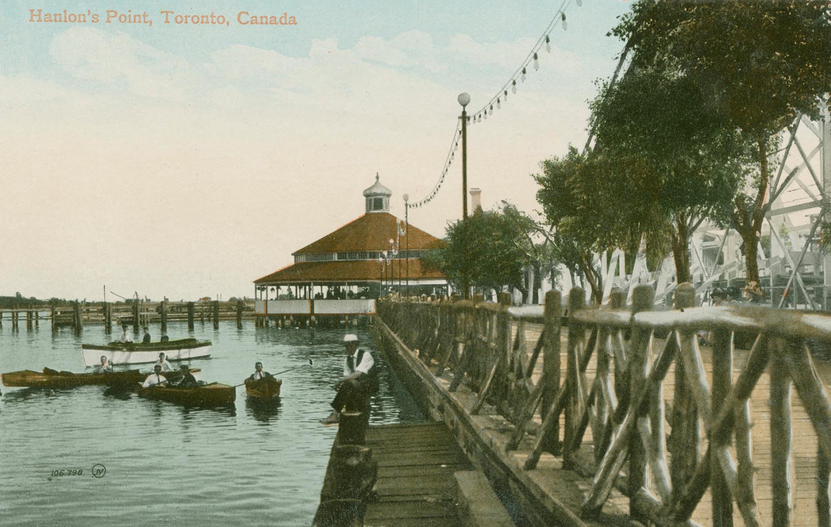 Picture of boardwalk on the right with amusement park building at the end and lake and boaters …