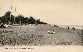 Picture of two children on a wide beach with other people in the background, trees and telephon…