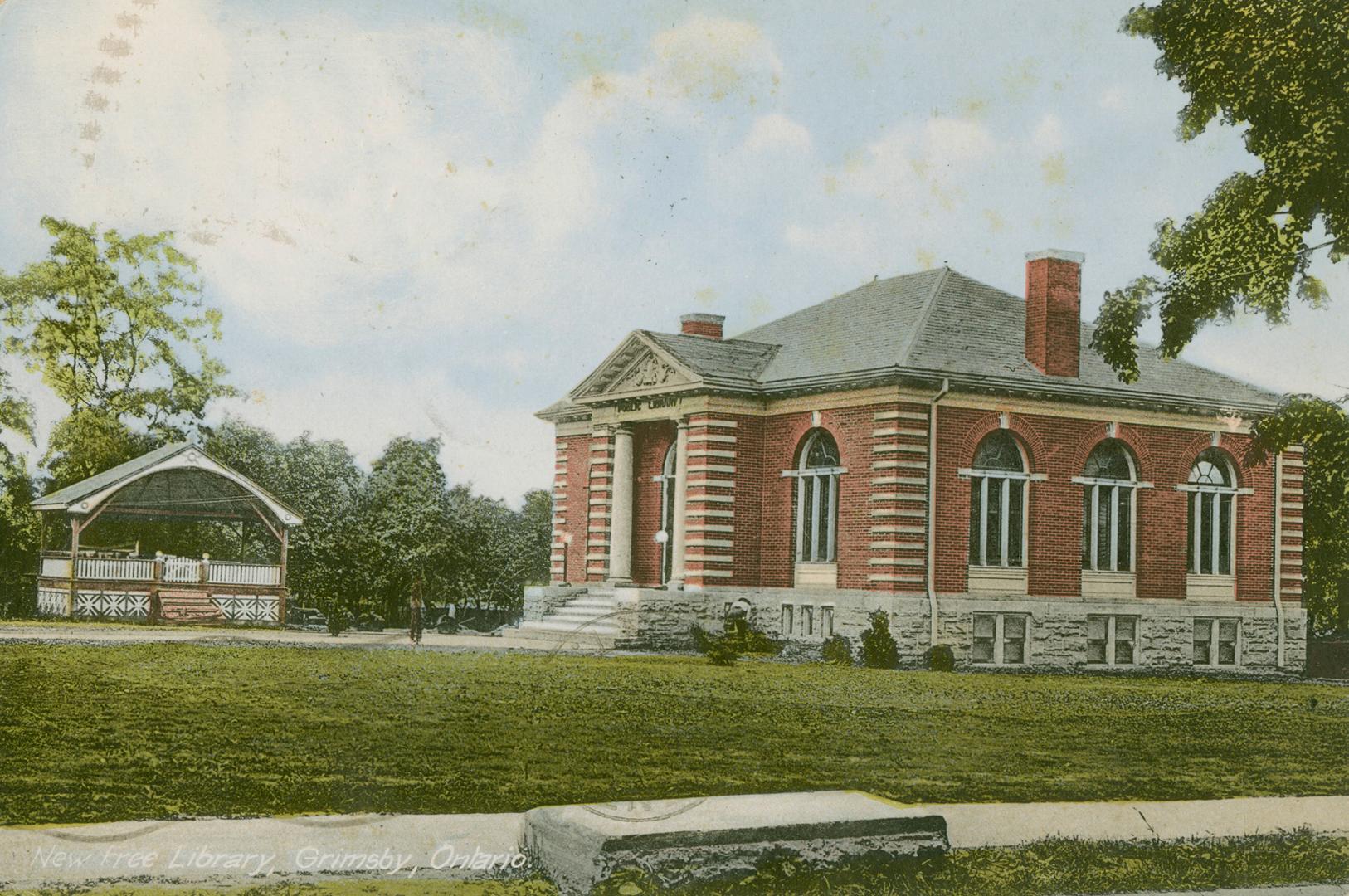 Picture of red brick single storey library with two front pillars and large lawn at front and a…