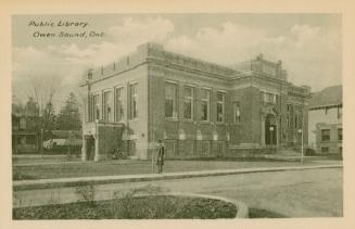 Picture of street scene with large public library with man standing outside and houses to the r…