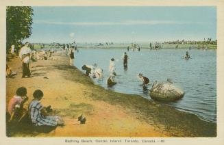 Picture of people at a beach with some sitting on the sand and some in the water. 