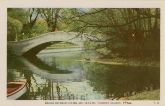 Bridge over body of water with a person on the bridge and row boat in the water. 