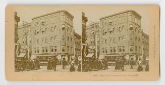 Pictures show pedestrians and a streetcar on a very busy street with tall buildings on either s…