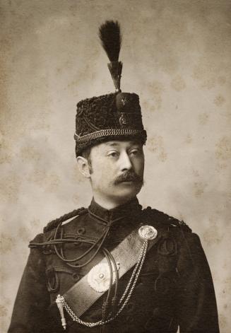 A formal photograph of a middle-aged man, taken in a studio. The man is balding, has a moustach…