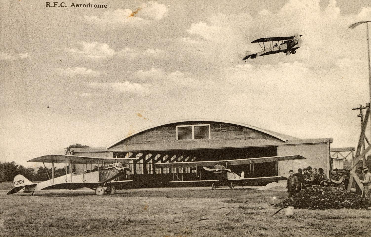 Sepia tone picture of two airplanes on the ground in front of a large, commercial building. Ano…