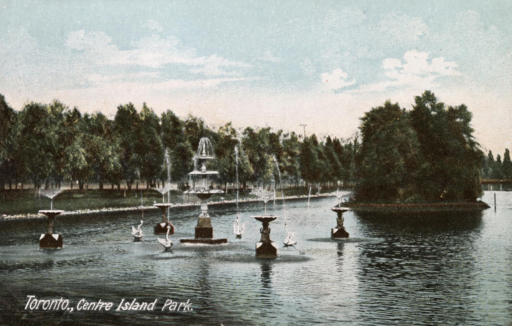 Swans, fountains and a small island within a narrow body of water.