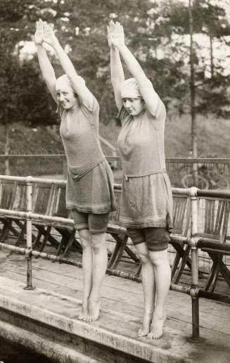 Black and white picture of two women in bathing suits preparing to dive into a swimming pool.