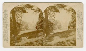 Pictures show a large collegiate building off in the distance. Man standing on a grassy hill be…