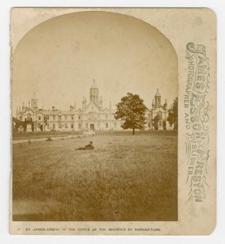 Half a stereoscope slide showing a man sitting on the lawn in front of a large building in the …