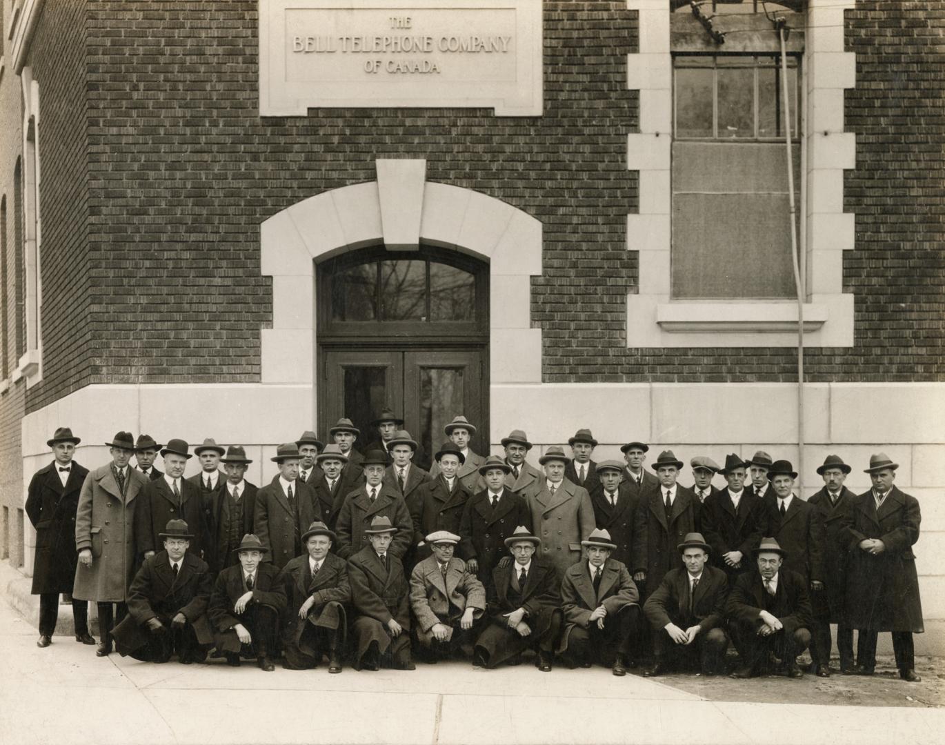 A photograph of approximately fifty people, all of whom appear to be men, standing and crouchin…