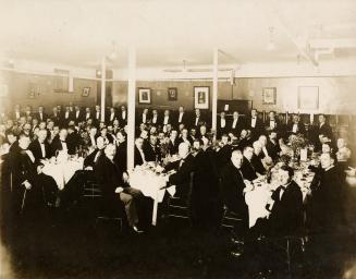 A photograph of a large group of people, who all appear to be men, dressed in formal clothing a…