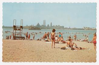 Color photograph of people in bathing suits on a sandy beach.